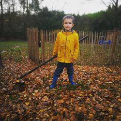 Portrait of boy holding rake standing in yard during autumn