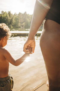 Woman holding hand of son while standing near lake on sunny day