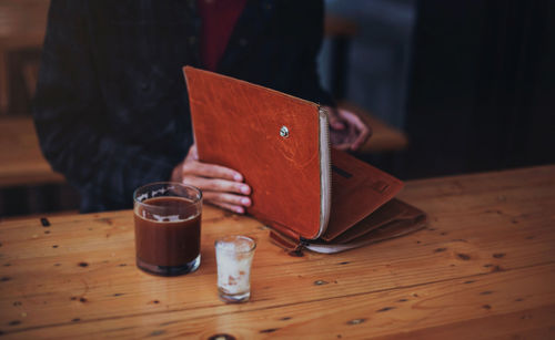 Midsection of woman holding folder by coffee in glass on table