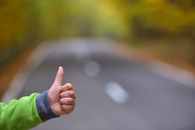 Cropped hand of child gesturing thumbs up sign over road