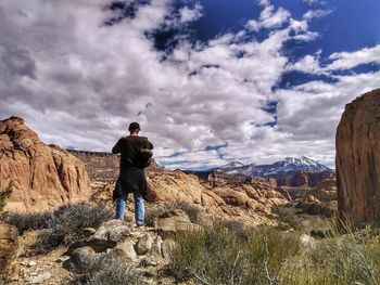 Rear view of hiker standing amidst rock formations against cloudy sky