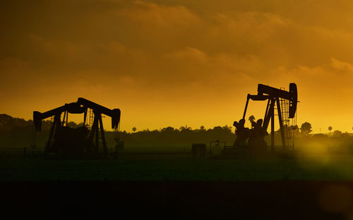 Oil wells on land against sky during sunset