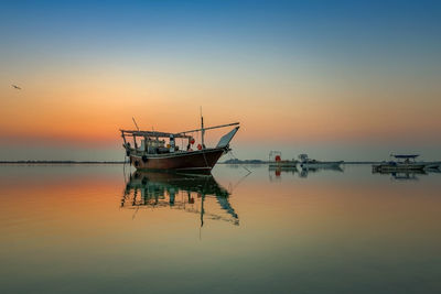 Fishing boat moored in sea against sky during sunset