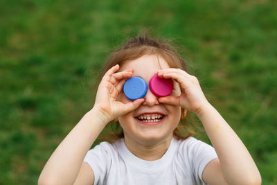 Close-up of smiling girl holding bottle caps on eyes