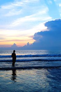 Rear view of man standing at beach against sky during sunset