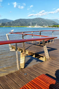 Empty deck chairs by lake against sky