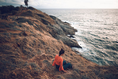 Woman sitting on mountain by sea