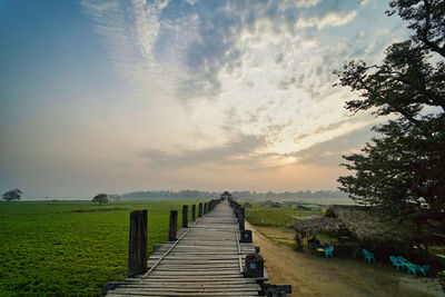 Empty footpath amidst field against sky during sunset