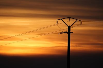 Low angle view of silhouette electricity pylon against dramatic sky during sunset
