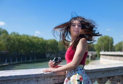 Beautiful woman with tousled hair standing on footbridge against sky