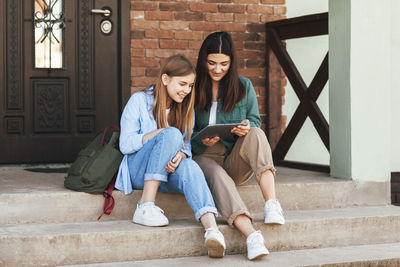 On the steps near the house, two beautiful girls-sisters who have come from the university