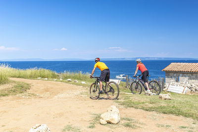 People riding bicycle by sea against sky