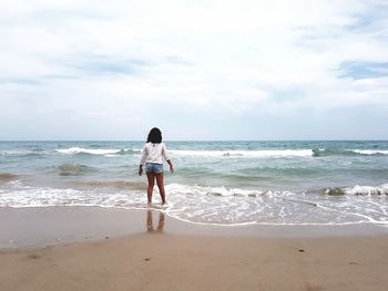 Rear view of woman standing in sea against sky