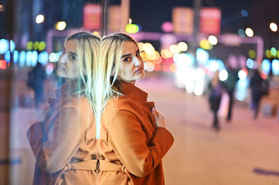 Woman standing by illuminated street at night