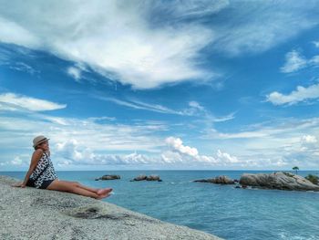 Woman sitting by sea against sky