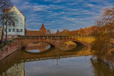 Arch bridge over river by buildings against sky