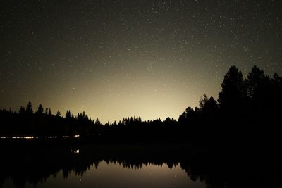 Silhouette trees by lake against clear sky at night