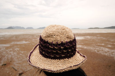 Rear view of woman wearing hat on sand at beach against sky