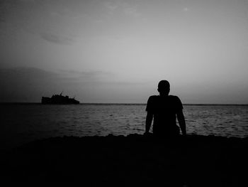 Silhouette man sitting on beach against sky