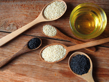 White and black sesame seeds in wooden spoon and a glass of oil