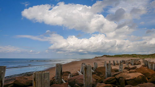 Stretch of red sand beach with fluffy cloud and old breakwater.