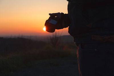 Midsection of man photographing against sky during sunset