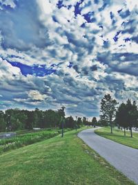 Road passing through field against cloudy sky