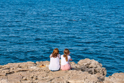 Rear view of women sitting on rock at beach