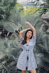Young woman with arms raised standing against plants