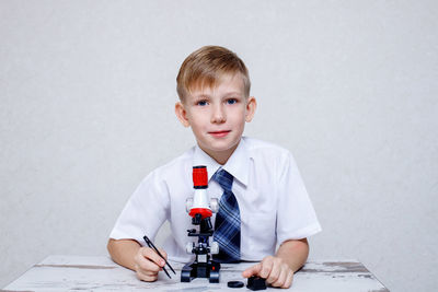 Portrait of smiling boy holding table against white background