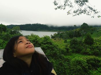 Portrait of young woman looking at trees against sky