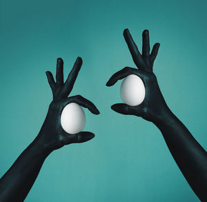 Cropped image of painted hands holding eggs against wall