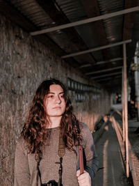 Young woman looking away while standing against wall