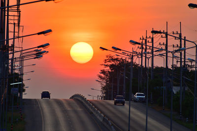 Cars on road against orange sky during sunset