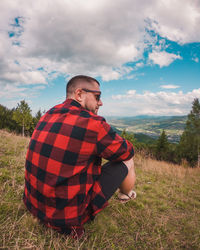 Rear view of man sitting on field against sky. traveller in the mountains