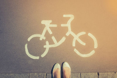 Low section of woman standing by bicycle sign on road