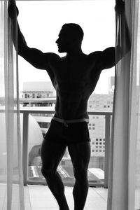 Rear view of shirtless man standing against window