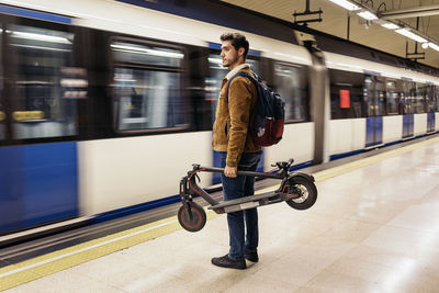 Full length of man with electric push scooter standing on subway station