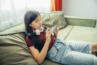 Side view of young woman looking away while sitting on sofa at home