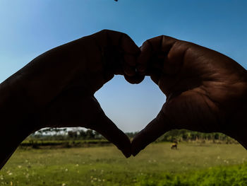 Person hand holding heart shape against clear sky