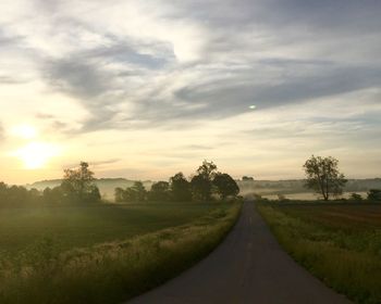 Road amidst field against sky during sunset