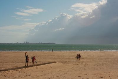 People at beach against cloudy sky