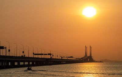 Silhouette bridge over sea against orange sky