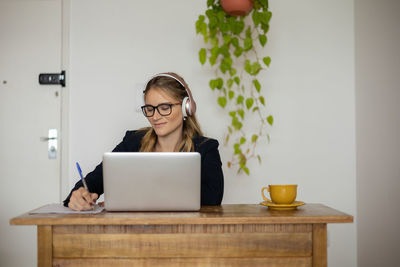 Woman working at home with laptop and papers on desk and headphones. home office . gray notebook 