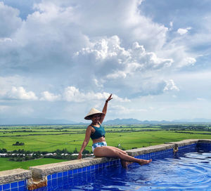 Full length of woman sitting by swimming pool against sky