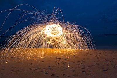 Illuminated light painting over sand at beach against sky during night