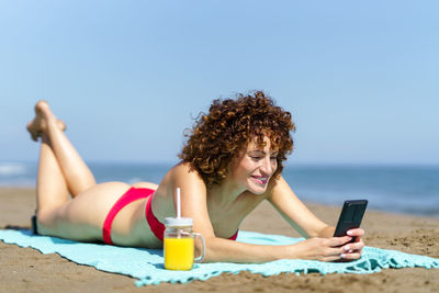 Side view of young woman sitting at beach against clear sky