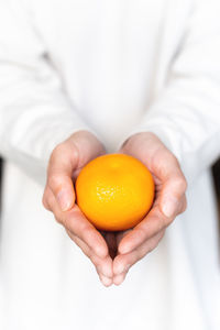 Girl in a white sweater holds a fresh sweet tangerine against the background of herself in defocus