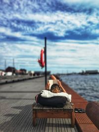 Woman reading book while lying at harbor against sky