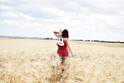 Young woman with ukulele on field against sky